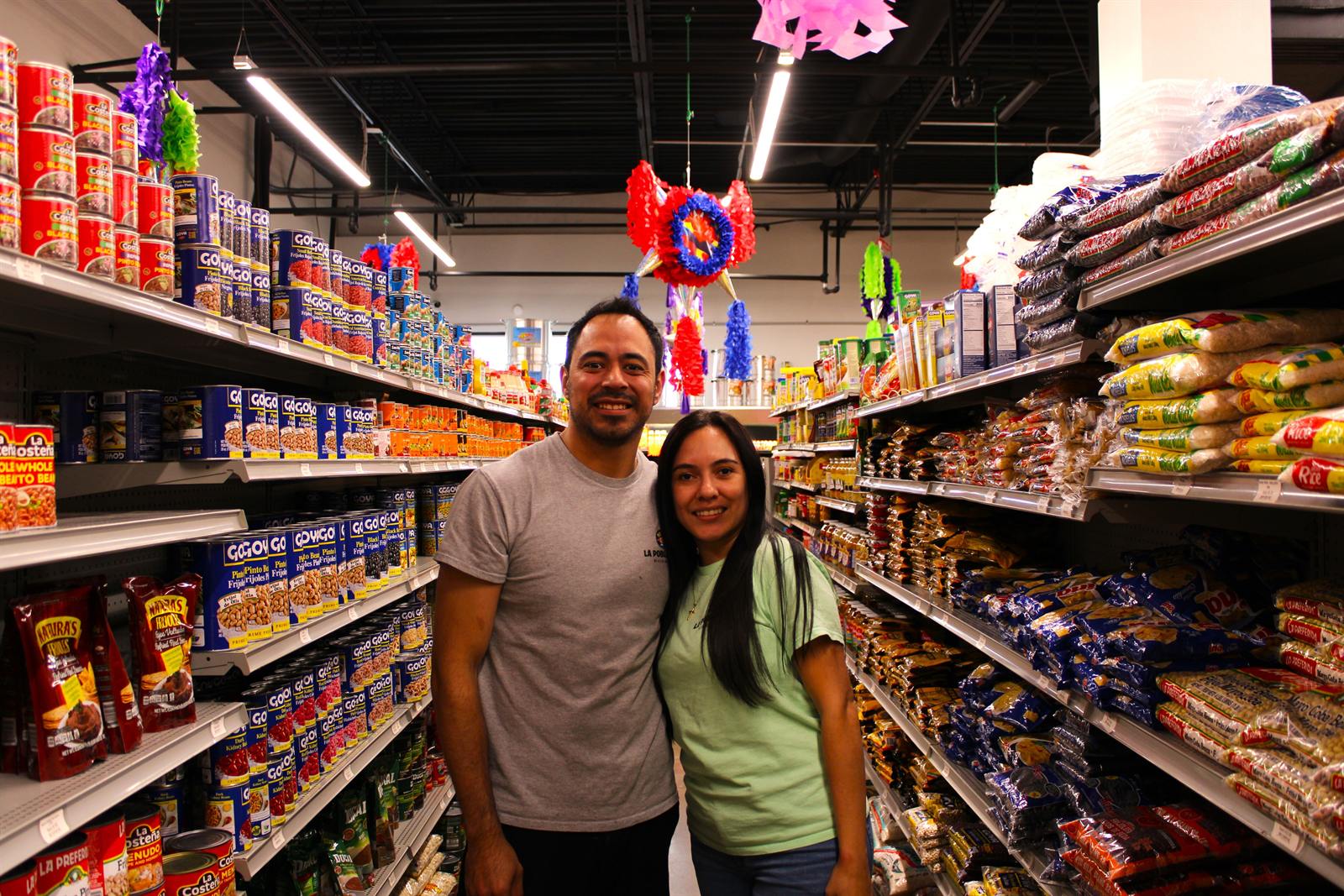 Shoppers in the La Poblanita aisle beneath hanging piñatas